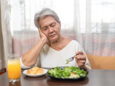 A woman rests her head on her hand with eyes closed as she eats a salad.