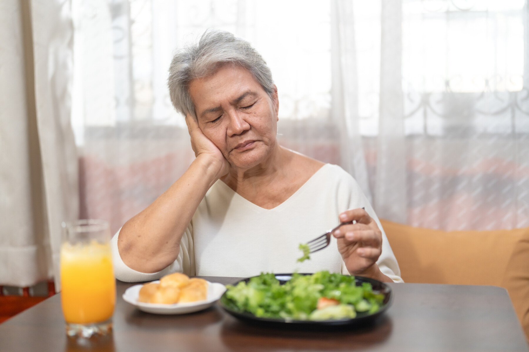A woman rests her head on her hand with eyes closed as she eats a salad.